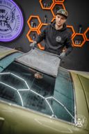 Black Master Drying Towel – Tattooed detailer smiling while drying olive-green car with the black premium towel in orange hex studio | Car Detailing | miio Store