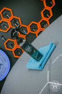 Quick Detailer 500ml – Flat-lay product shot: black bottle on grey surface with orange hexagonal backdrop and blue microfibre cloth | Car Detailing | miio Store