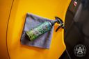 Ceramic Detailer 500ml – Green-labelled bottle leaning against yellow car door panel with grey microfibre cloth draped over it | Car Detailing | miio Store