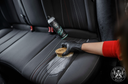 Fabric Cleaner – Braço com manga vermelha a escovar tecido escuro de assento com escova redonda, frasco ao fundo | Interior Auto | miio Store