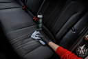 Fabric Cleaner – Mão com luva a usar escova redonda para limpar estofos de assento auto escuro, frasco próximo | Interior Auto | miio Store