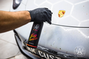 Bug Remover 1L – Gloved hand spraying product on grey car bonnet with Porsche badge visible in JK Customs detailing studio | Car Detailing | miio Store